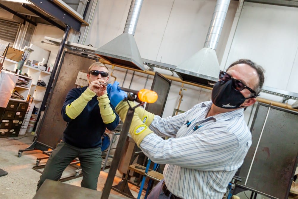 BespokeCoursesImg Two people wearing safety gear shape molten glass in a workshop.